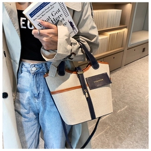 Detail of canvas bucket bag with leather trim held by a model in a casual setting