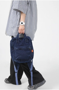 Detailed view of dark blue denim backpack with orange label and light blue straps