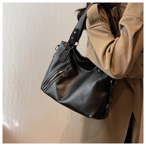 Detail of a black pebbled leather tote bag with side zippers and silver ring hardware