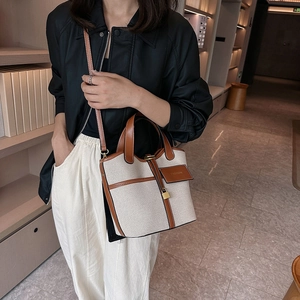 Detail of canvas bucket bag with brown leather trim and golden padlock charm worn by model
