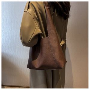 Gros plan d'un sac cabas en cuir marron porté par un modèle en trench-coat
