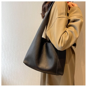 Détail d'un sac cabas noir en cuir grainé porté par un mannequin en trench-coat