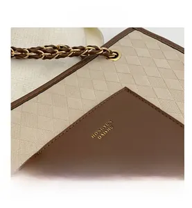 Détail d'un sac en tissu matelassé beige avec poche en cuir marron et chaîne dorée