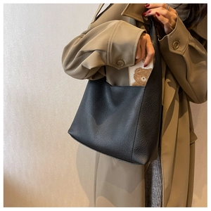 Détail d'un sac à main noir à motif litchi porté avec un trench-coat kaki élégant