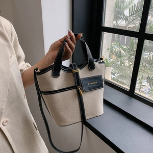 Close-up of canvas bucket bag with black leather trim, contrast stitching and fashion patch