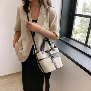 Detail of canvas bucket bag with black leather trim and fashion lock worn by a model
