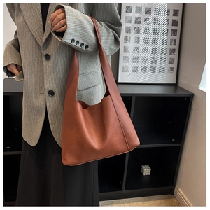 Détail d'un sac hobo en cuir grainé marron foncé porté avec un blazer élégant