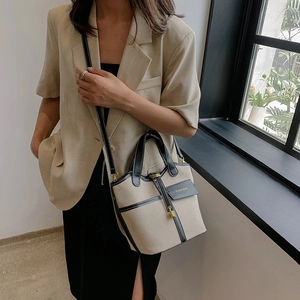 Close-up of beige canvas and black leather bucket bag worn with a chic blazer