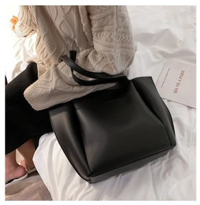 Macro detail of a black soft PU leather tote bag on white bedding with warm lighting