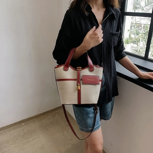 Woman wearing a beige canvas bucket bag with burgundy leather trim and gold lock detail