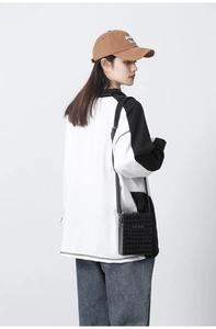 Side view of a black crocodile-patterned crossbody bag on a model in casual wear