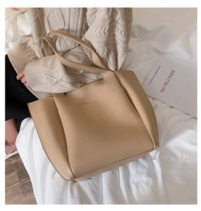 Detail of a large beige PU leather tote bag with functional front pocket on model lap