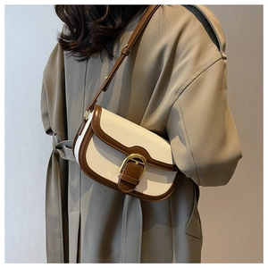 Detail of cream and brown saddle bag with golden clasp worn with a khaki trench coat