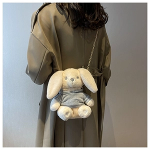 Détail du sac bandoulière lapin en peluche avec chaîne dorée sur un trench-coat kaki