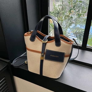 Detail of canvas bucket bag showing navy leather trim, gold lock, and fashion tag