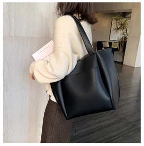 Rear view of a model wearing a large black matte PU tote bag with a wide shoulder strap