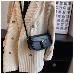 Close-up of black retro saddle bag featuring gold horseshoe buckle on beige corduroy suit