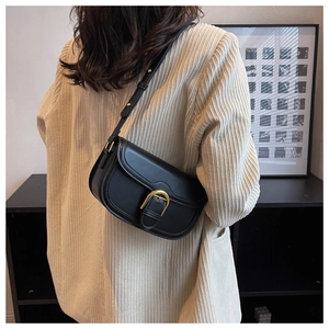 Detail of vintage black saddle bag with gold metal U-buckle on beige blazer outfit