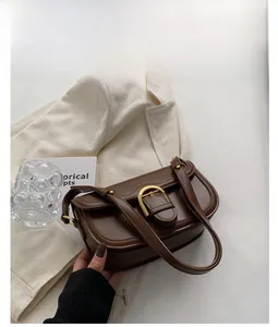 Detail of coffee brown saddle bag featuring a gold horseshoe buckle on white suit