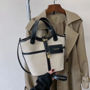 Detail of canvas bucket bag with black leather trim and metal lock on trench coat background