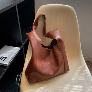 Sac fourre-tout marron texture litchi présenté sur une élégante chaise beige