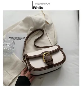 Detail view of white saddle bag with brown trim and gold horseshoe metal buckle closure