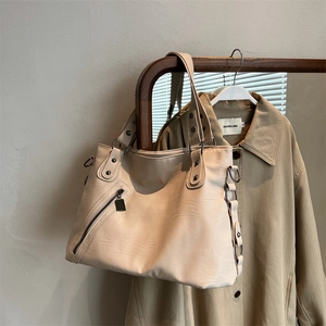 Minimalist beige oversized tote bag with side zipper and metal rivets on a wooden stand