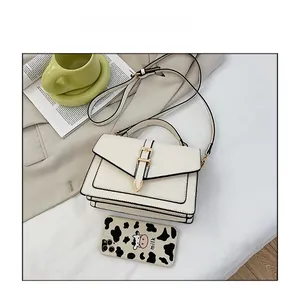 Cream-colored square crossbody bag with black trim and gold clasp next to a phone case
