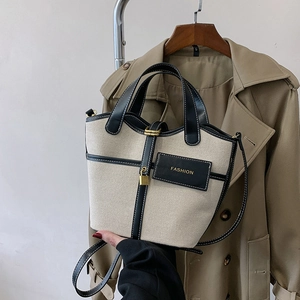 Detail of canvas bucket bag with black leather trim and gold lock worn with a trench coat