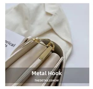 Close-up of golden metal hooks and accordion side gussets on a beige PU leather crossbody bag