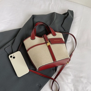 Detail of canvas bucket bag with burgundy leather trim and gold buckle on a blazer
