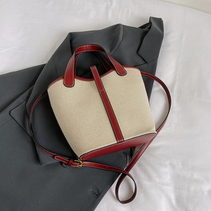 Detail of canvas bucket bag with burgundy leather trim and white contrast stitching