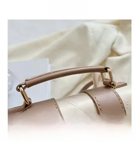 Detailed macro view of cream geometric quilted leather bag with brown handle and gold hardware
