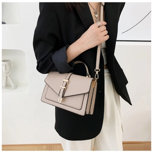 Detail view of beige crossbody bag with gold buckle on model in minimalist gallery