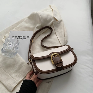 Vintage saddle bag in white and brown with a gold horseshoe buckle on an ivory blazer