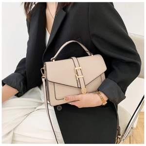 Close-up of beige crossbody bag with gold buckle detail shown with elegant outfit