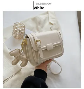 Detail of white leather crossbody bag with gold buckle and cute leather bear charm