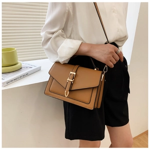 Close-up of a brown leather crossbody bag with gold buckle on a minimalist background