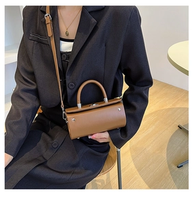 Brown cylindrical crossbody bag with top handle and strap styled on a blazer