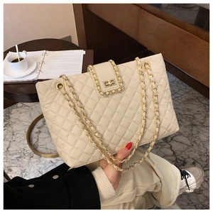 Elegante borsa tote beige trapuntata con tracolla a catena d'oro su tavolo in legno
