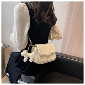 Chic cream crossbody flap bag with a cute puppy pendant shown on a model
