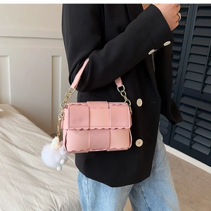 Close-up of pink woven leather shoulder bag with scalloped edges and plush white pompom