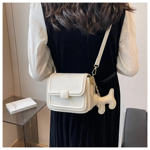 Detail of cream white crossbody bag with square buckle and cute dog charm on model