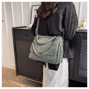 Green matte textured tote bag with chain detail shown on a model in a natural setting