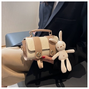Detail of beige quilted cylinder bag with a gold twist lock and cute plush rabbit charm