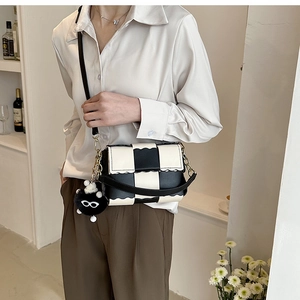 Detail of checkered shoulder bag with wavy edges and a cute black plush charm