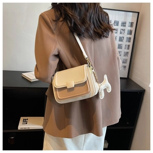 Side view of a beige and brown color-block crossbody bag with a plush charm accessory