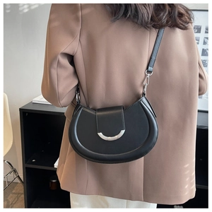 Détail d'un sac demi-lune noir avec boucle argentée porté sur un blazer marron élégant