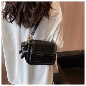 Detail of black crossbody bag with white stitching and 3D puppy charm accessory
