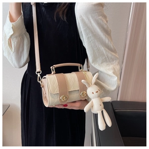 Detail of cream quilted cylindrical crossbody bag featuring a cute rabbit charm and twist lock